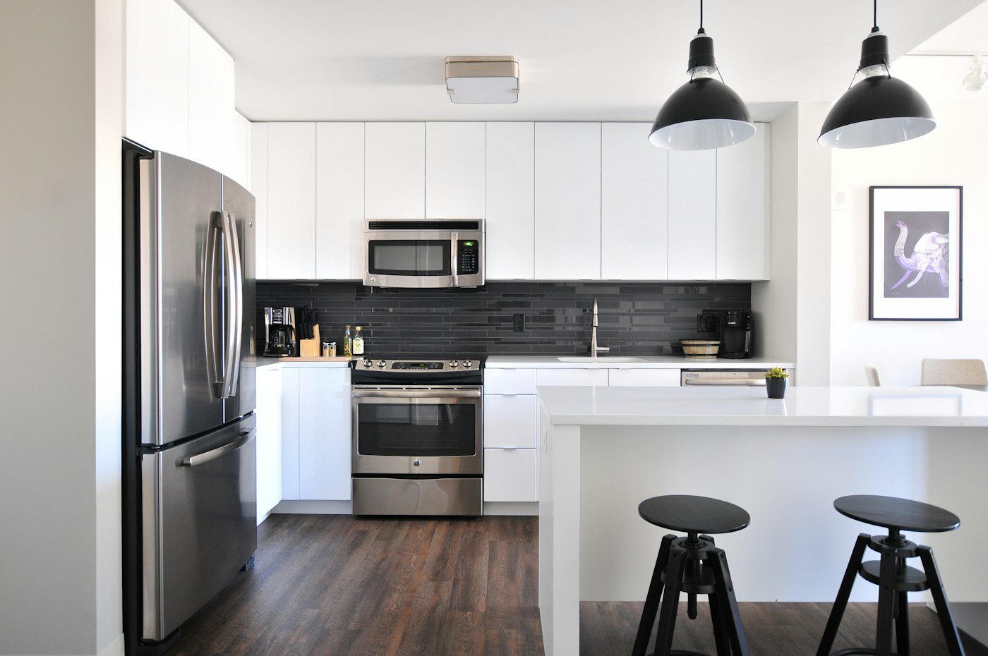 A white kitchen with stainless appliances, pendant lights and an island with stools
